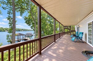 A covered deck with a view of a lake, wooden railings, and outdoor furniture.