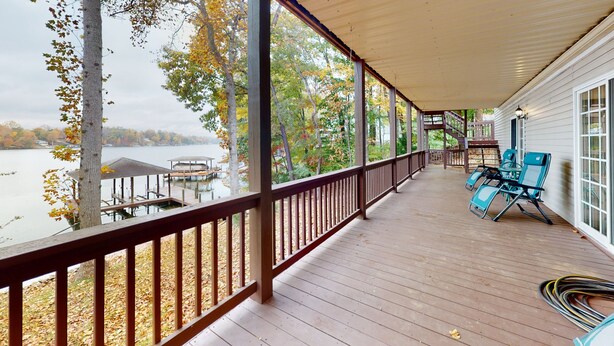 Une véranda couverte avec vue sur un lac, une terrasse en bois et du mobilier d’extérieur.