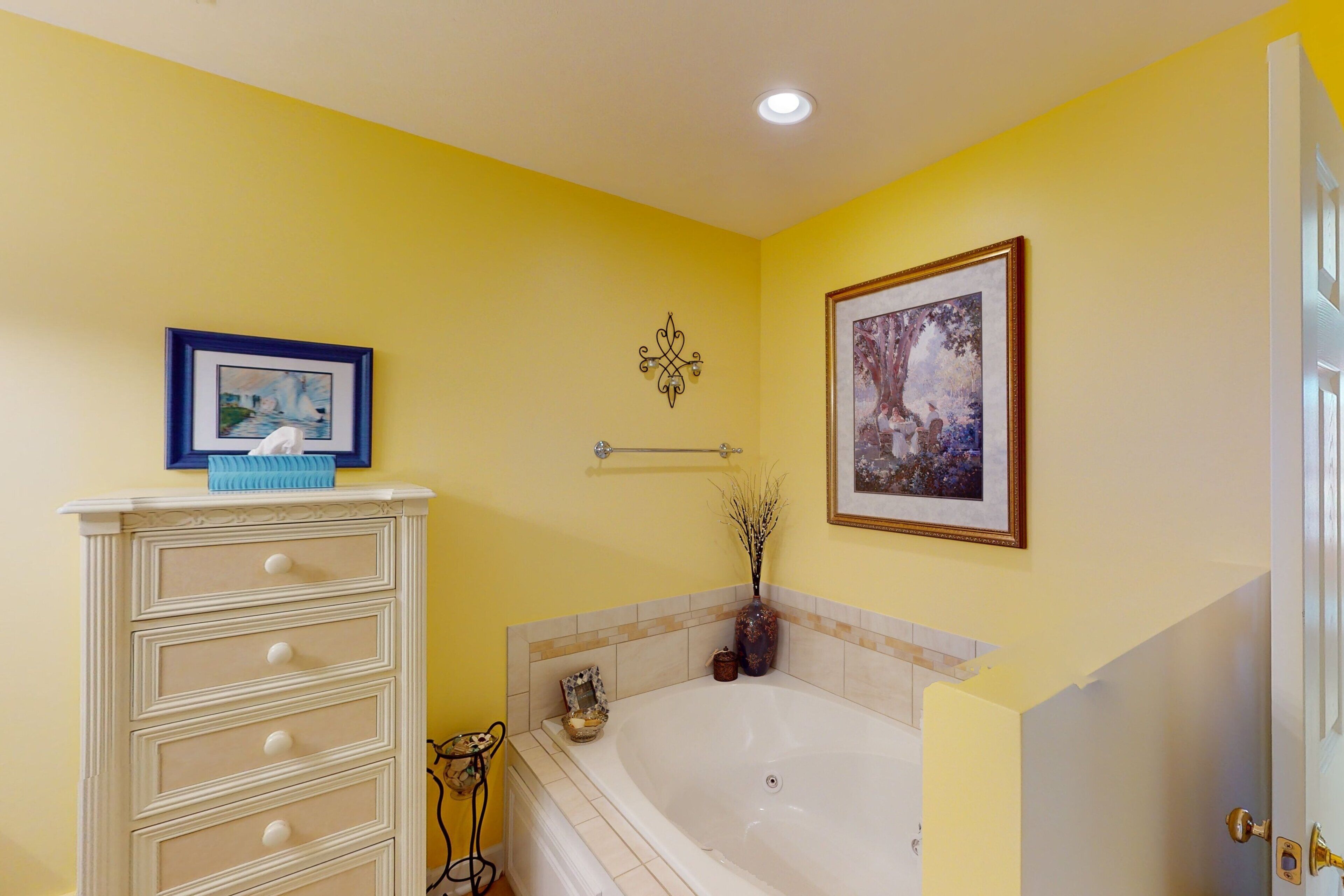 A bathroom with a bathtub, a vanity with drawers, a framed picture on the wall, and a decorative wall piece.