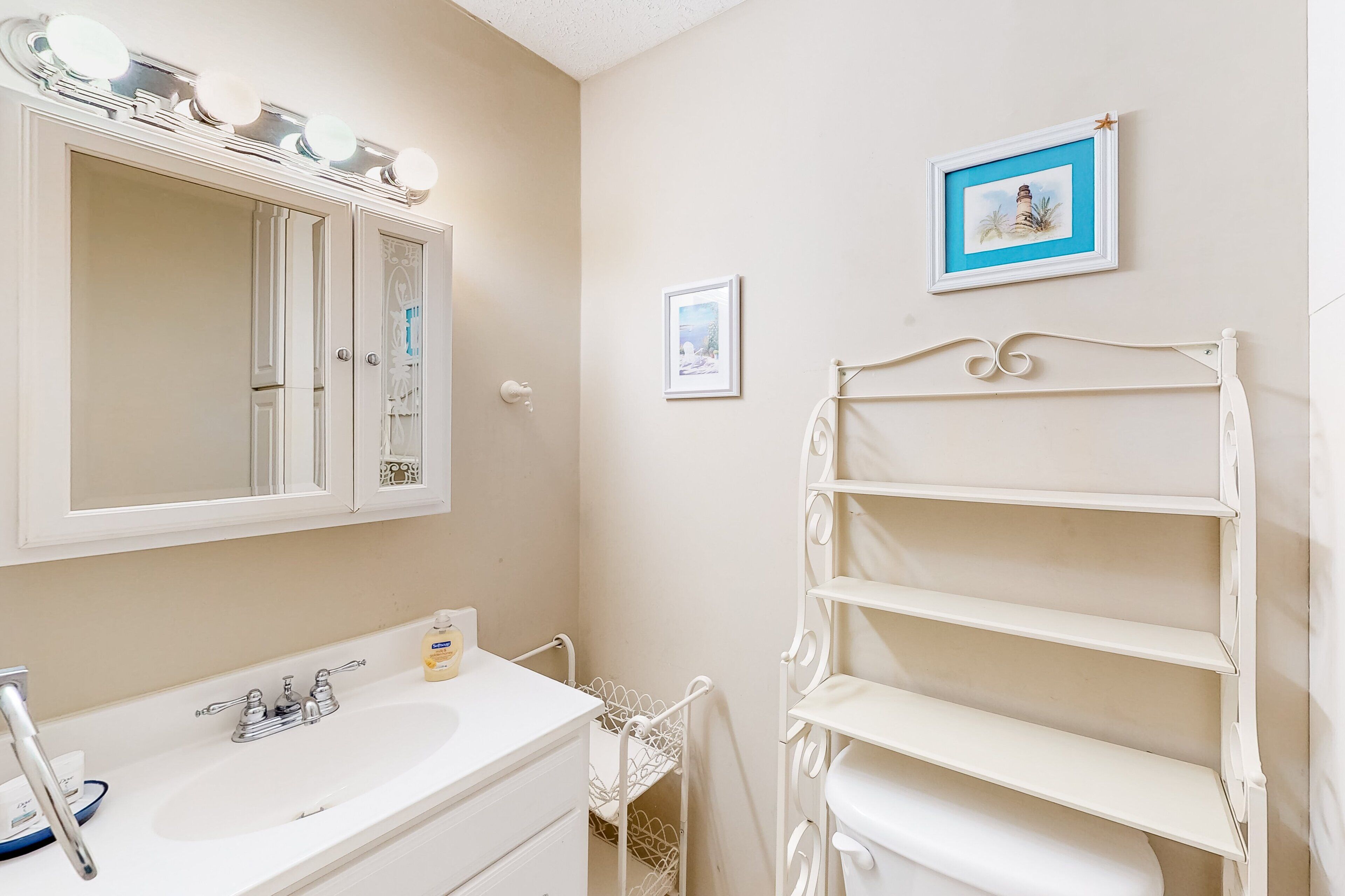 A bathroom with a white vanity, a mirror with lights, a sink, and a white towel rack.