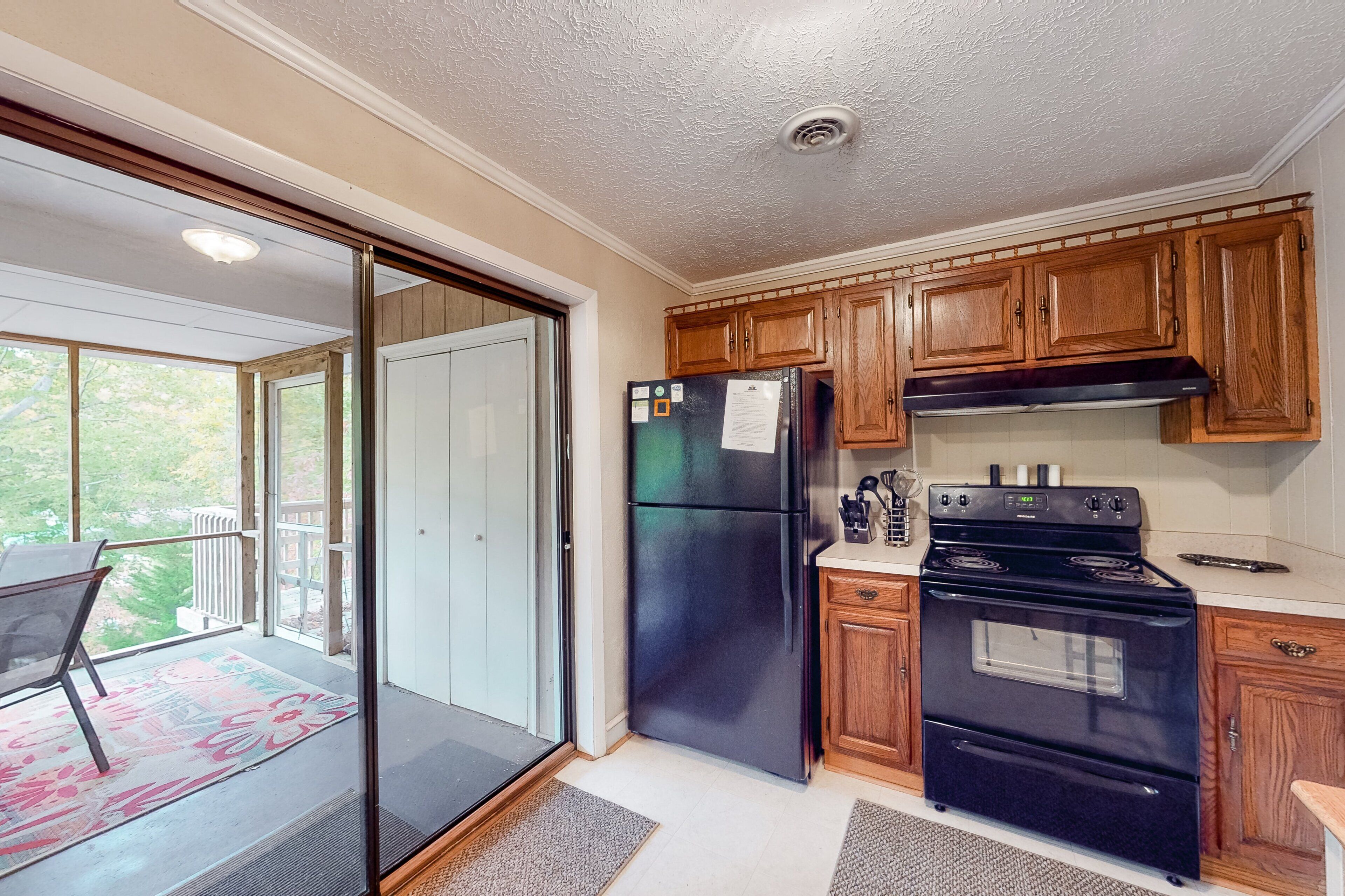 A kitchen with wooden cabinets, a black refrigerator, a stove, and a sliding glass door leading to a balcony.