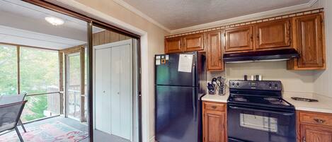A kitchen with wooden cabinets, a black refrigerator, a stove, and a sliding glass door leading to a balcony.