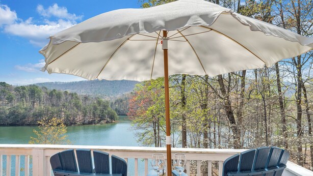 A deck with two chairs and an umbrella, overlooking a lake and forest. - Heron's Cove - Pet Friendly, Private Dock! (Huddleston)