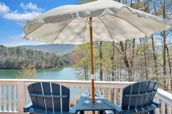 A deck with two chairs and an umbrella, overlooking a lake and forest. - Heron's Cove - Pet Friendly, Private Dock! (Huddleston)