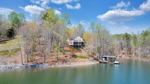 A lakeside property with a large house, dock, and surrounding forest. - Heron's Cove - Pet Friendly, Private Dock! (Huddleston)