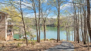 A lakeside cabin with a wooden deck, surrounded by trees and a clear view of the lake. - Heron's Cove - Pet Friendly, Private Dock! (Huddleston)
