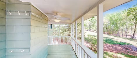 A covered porch with a ceiling fan, white railings, and a view of a wooded area.
