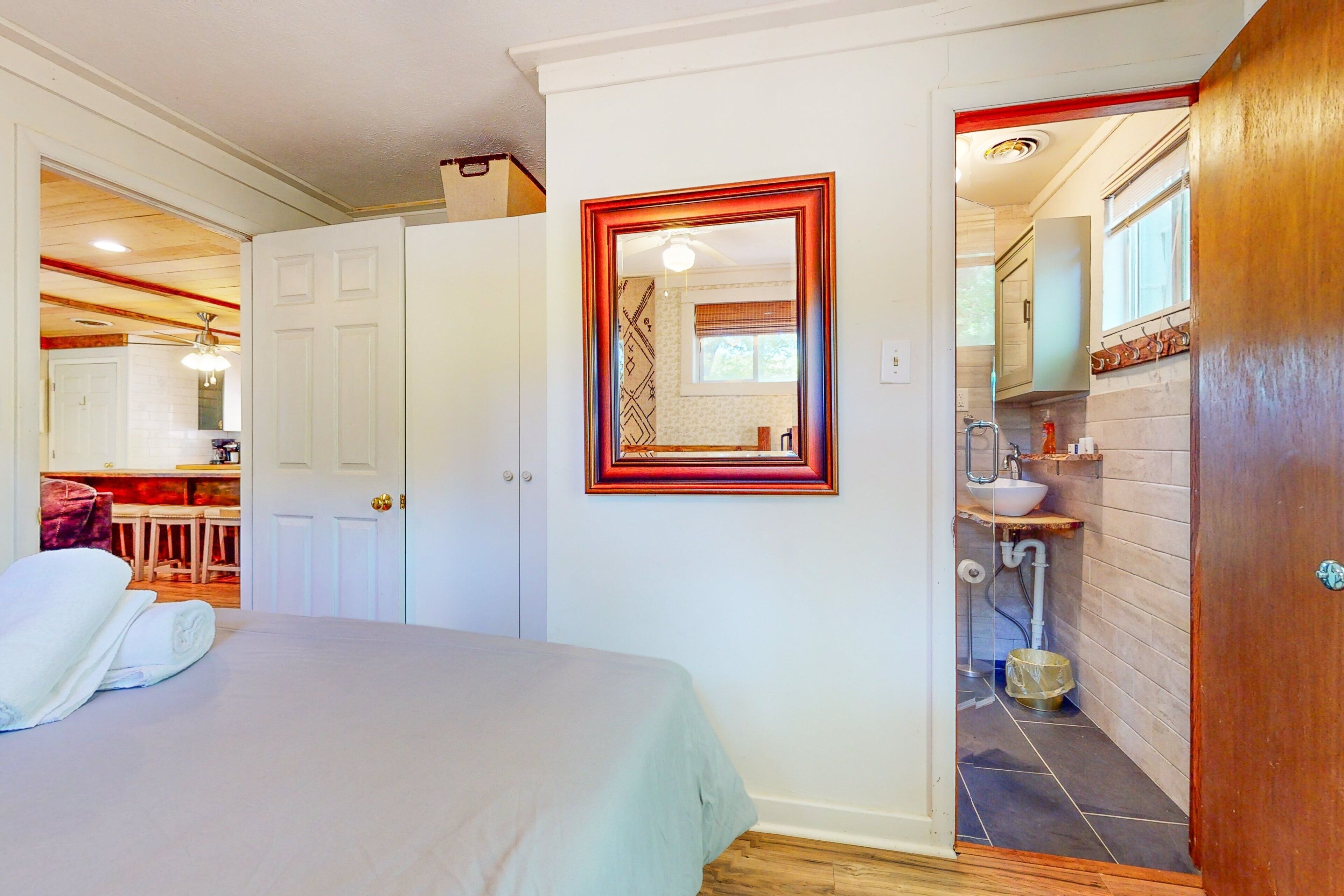 A bedroom with a bed, a bathroom with a sink, and a kitchen area visible through an open door.
