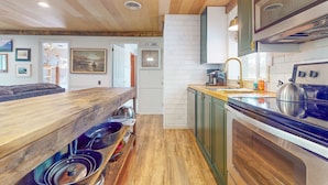 Une cuisine avec un plancher en bois, une cuisinière encastrée et une table à manger en bois, avec des bols rangés en dessous.