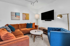 A modern living room with a sofa, armchair, TV, lamp, and artwork.