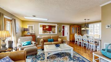 A spacious living room with a large sofa, a coffee table, and a dining area with white chairs.