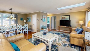 A living room with a sofa, coffee table, TV, and dining area with chairs and a table. - Smith Mountain Bliss - Spacious Waterfront House W/patio, Deck, Fire pit & Grill (Moneta)