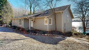 A single-story house with a sloped roof, a front porch, and a gravel driveway. - Smith Mountain Bliss - Spacious Waterfront House W/patio, Deck, Fire pit & Grill (Moneta)