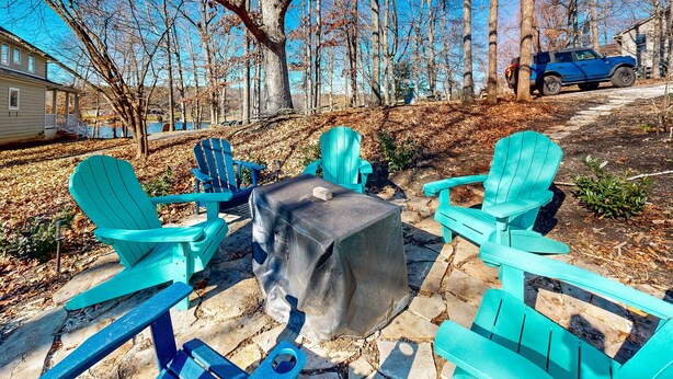 A patio with Adirondack chairs, a covered table, and a stone pathway. - Smith Mountain Bliss - Spacious Waterfront House W/patio, Deck, Fire pit & Grill (Moneta)