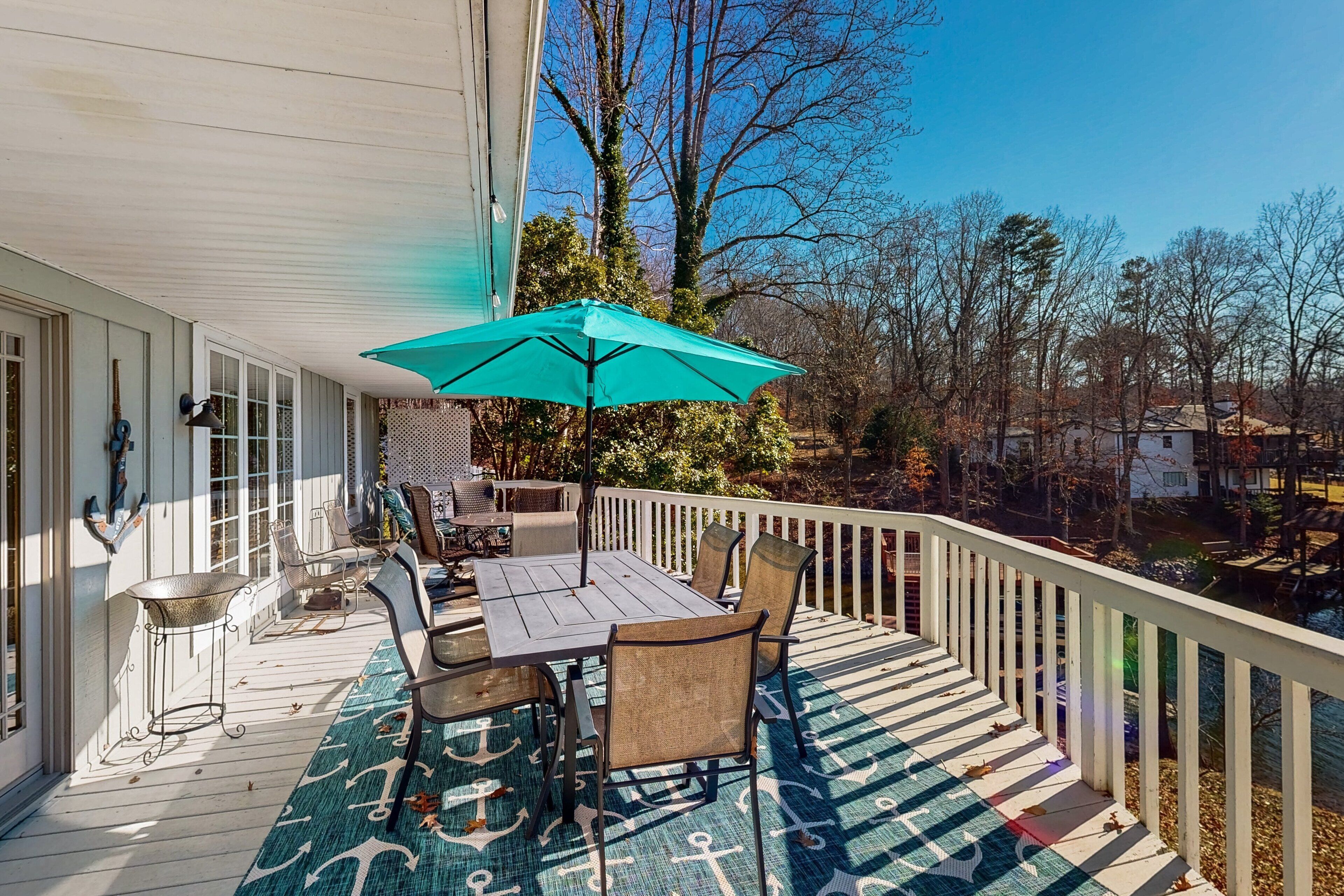 A covered outdoor deck with a table and chairs, a teal umbrella, and a patterned rug.