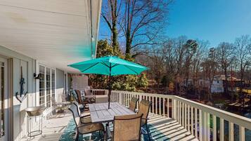 A covered outdoor deck with a table and chairs, a teal umbrella, and a patterned rug.