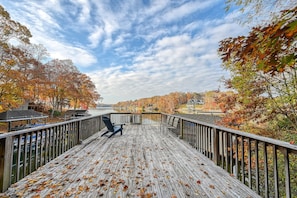 A wooden deck with a chair, overlooking a lake with autumn foliage. - SML Ski School - Pet Friendly Lake Lodge With Waterfront Deck, Firepit, & Game Room (Moneta)