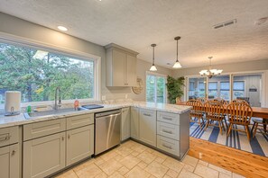 A modern kitchen with a dishwasher, large windows, and a dining area with wooden chairs. - Yellow Fellow - Lake House With hot Tub, Waterfront Deck, Swimming Cove & Firepit (Moneta)