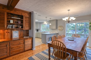 A wooden dining area with a large table and chairs, a chandelier, and a view of the backyard through large windows. - Yellow Fellow - Lake House With hot Tub, Waterfront Deck, Swimming Cove & Firepit (Moneta)