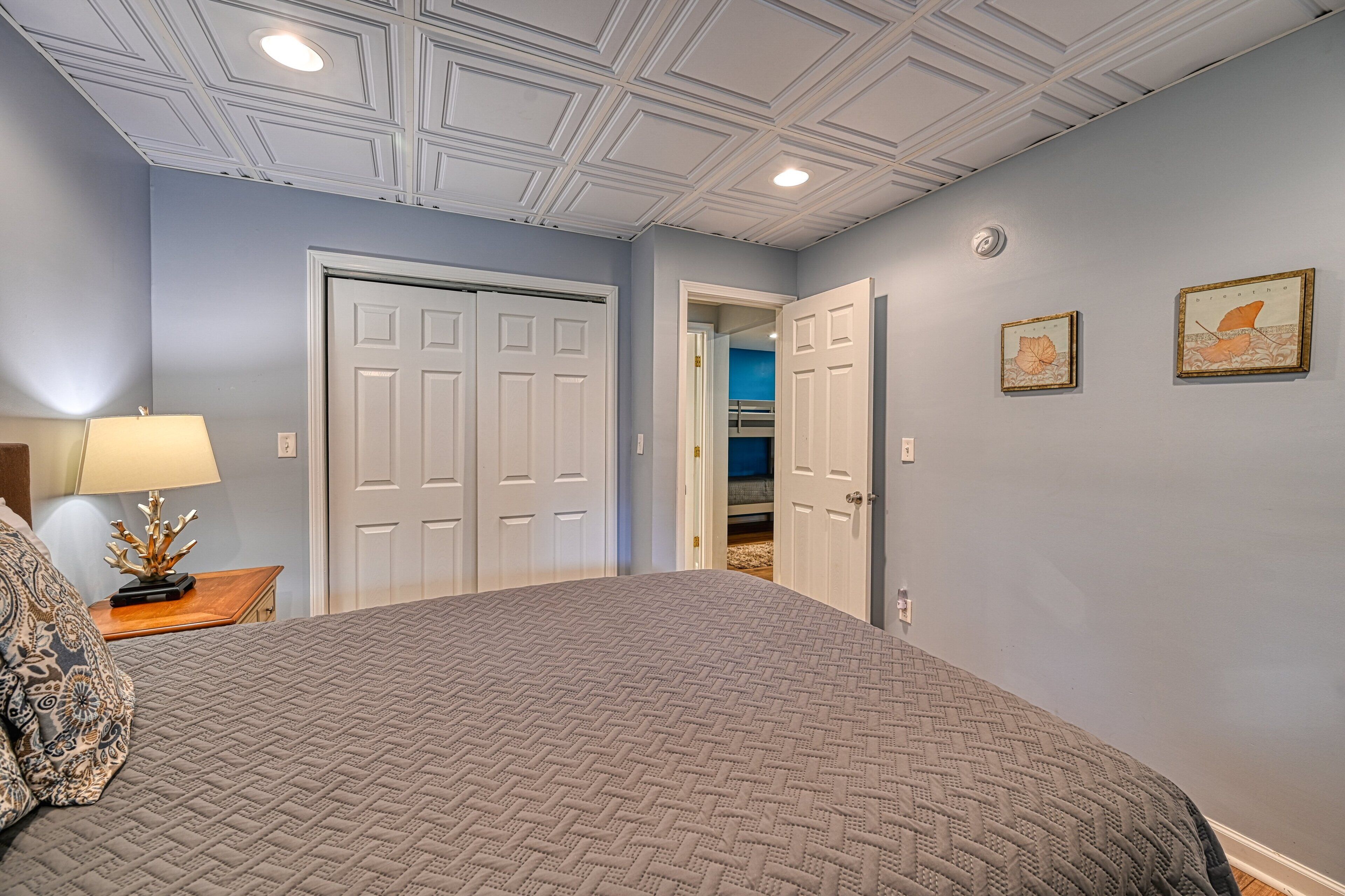 A bedroom with a bed, a nightstand, a lamp, and a door leading to a closet.