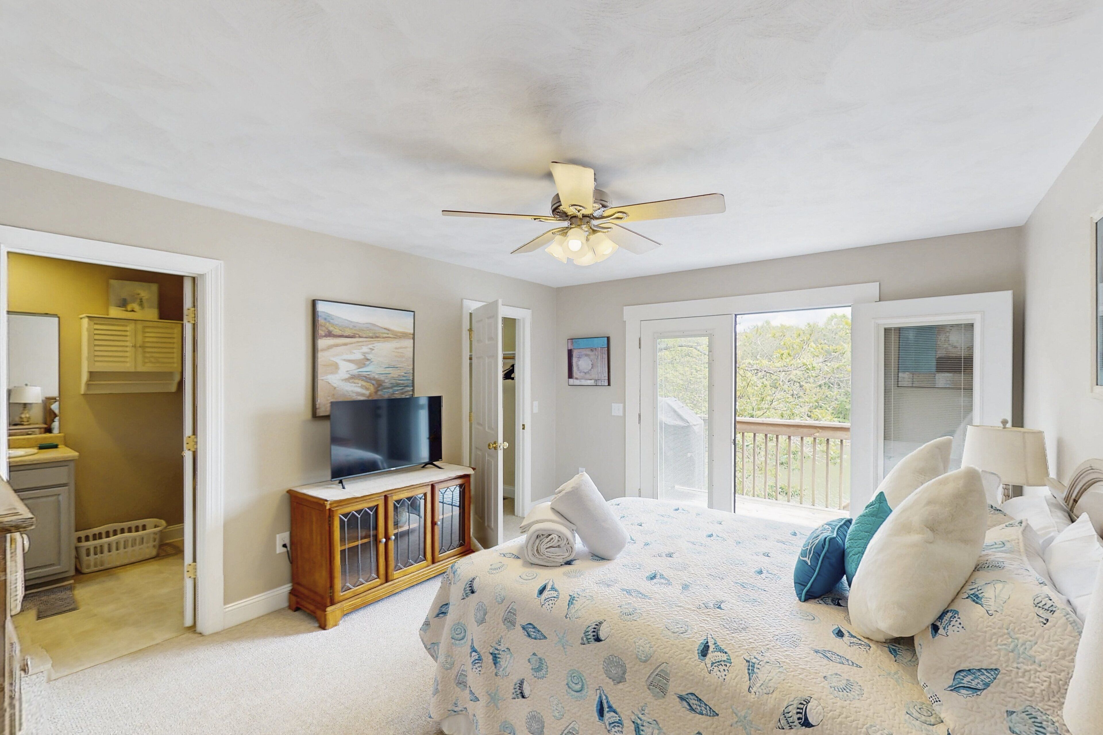 A bedroom with a bed, a ceiling fan, a television, and a view through the open door.