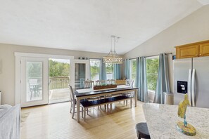 A spacious kitchen with a dining table, a refrigerator, and a large window with curtains. - Wet Feet Retreat - Beautiful Lake House With Incredible Views and Dock (Moneta)