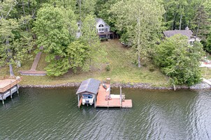 Una propiedad frente al lago con un muelle, un espacio cubierto para guardar barcos y una casa rodeada de árboles.