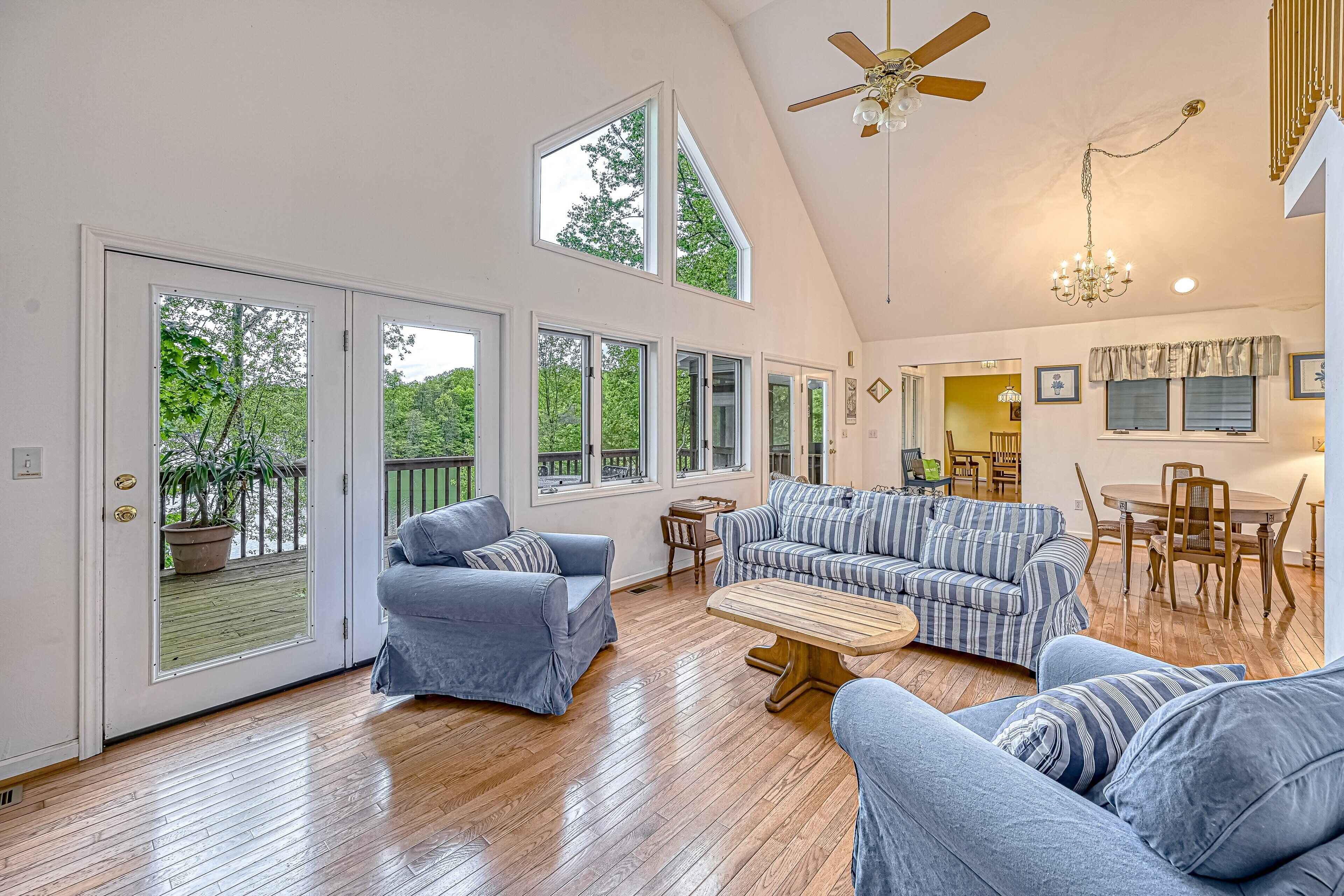 A spacious living room with a high ceiling, large windows, a ceiling fan, and a dining area.