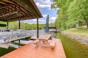 Un muelle de madera con una mesa de picnic, un espacio de estar cubierto y un bote amarrado al agua.