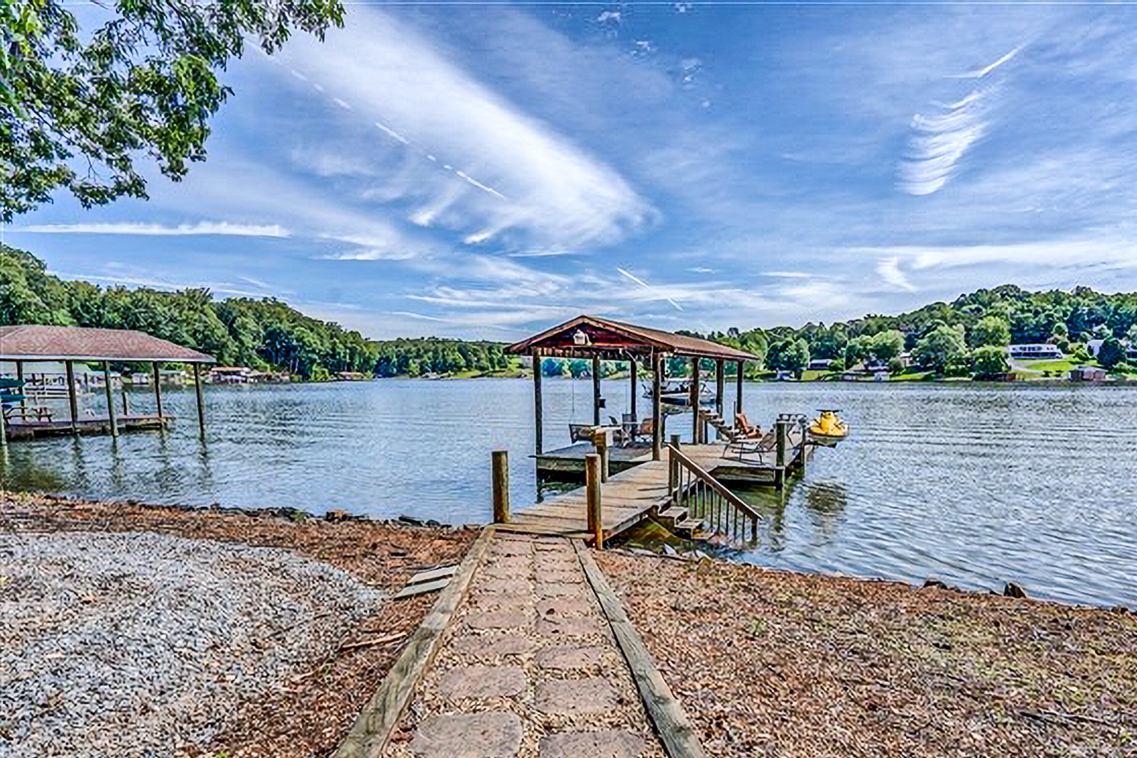 Une jetée au bord du lac, avec un espace de repos abrité, un bateau et un petit bâtiment en arrière-plan.