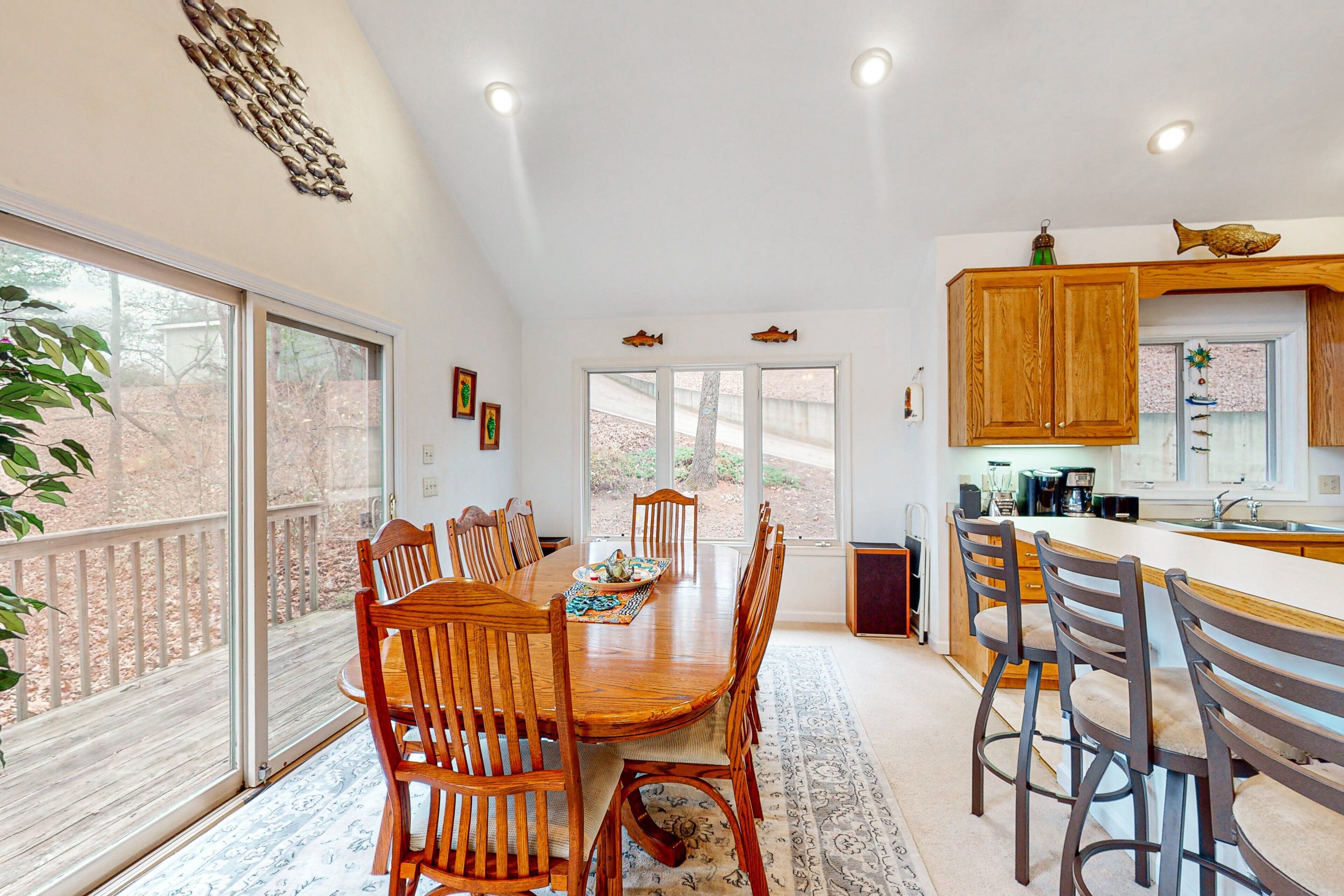 A spacious dining area with a large wooden table and chairs, a kitchen with wooden cabinets, and a view through large windows.