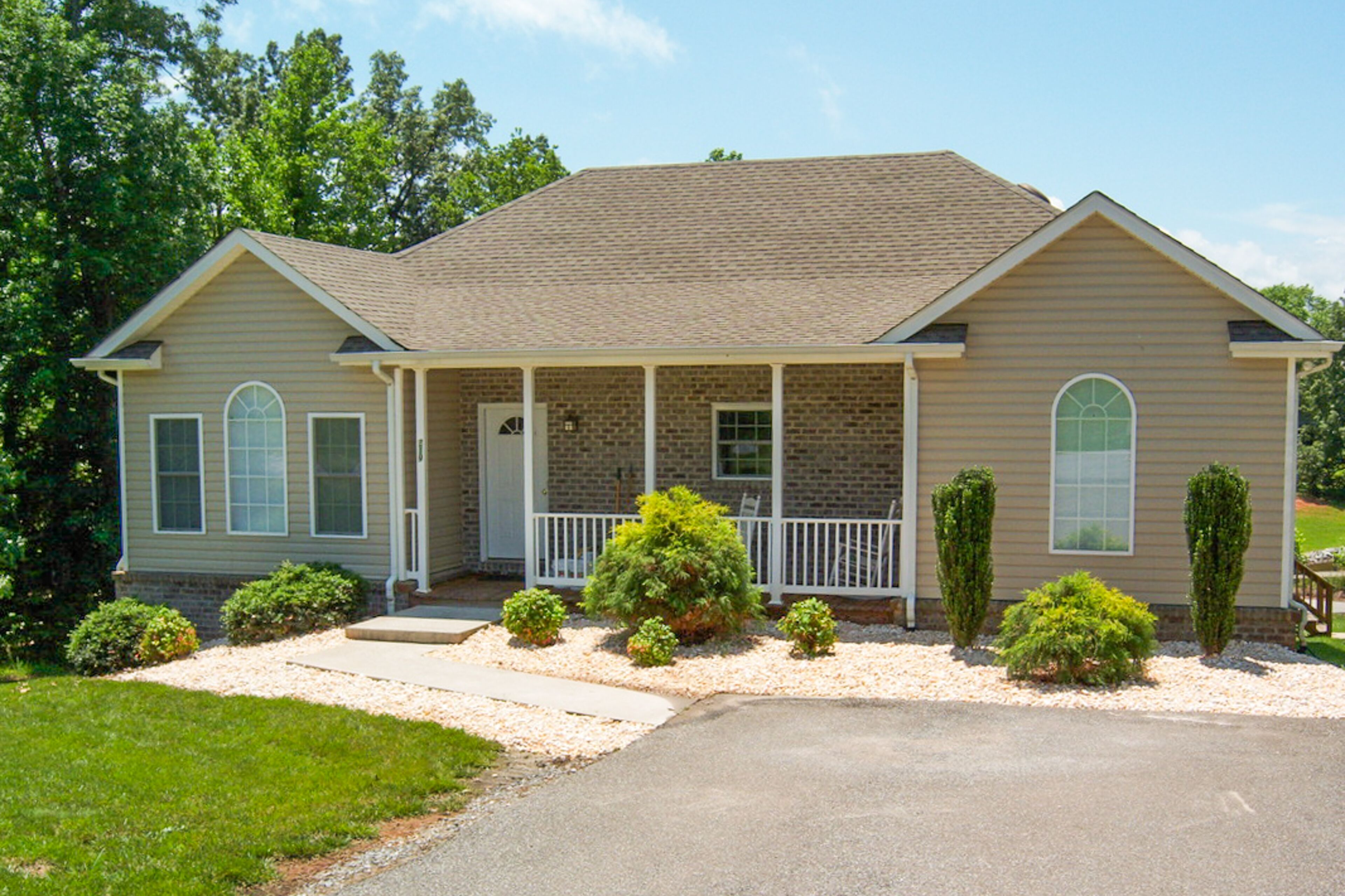 A two-story house with a front porch, brick exterior, and a driveway leading to a garage.