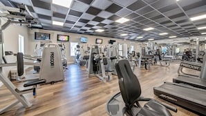 Ein Fitnessraum mit verschiedenen Trainingsgeräten, einem Laufband und einer Spiegelwand.