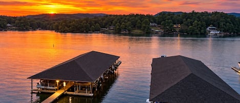 A waterfront property with two docked boats, a pier, and a sunset view.