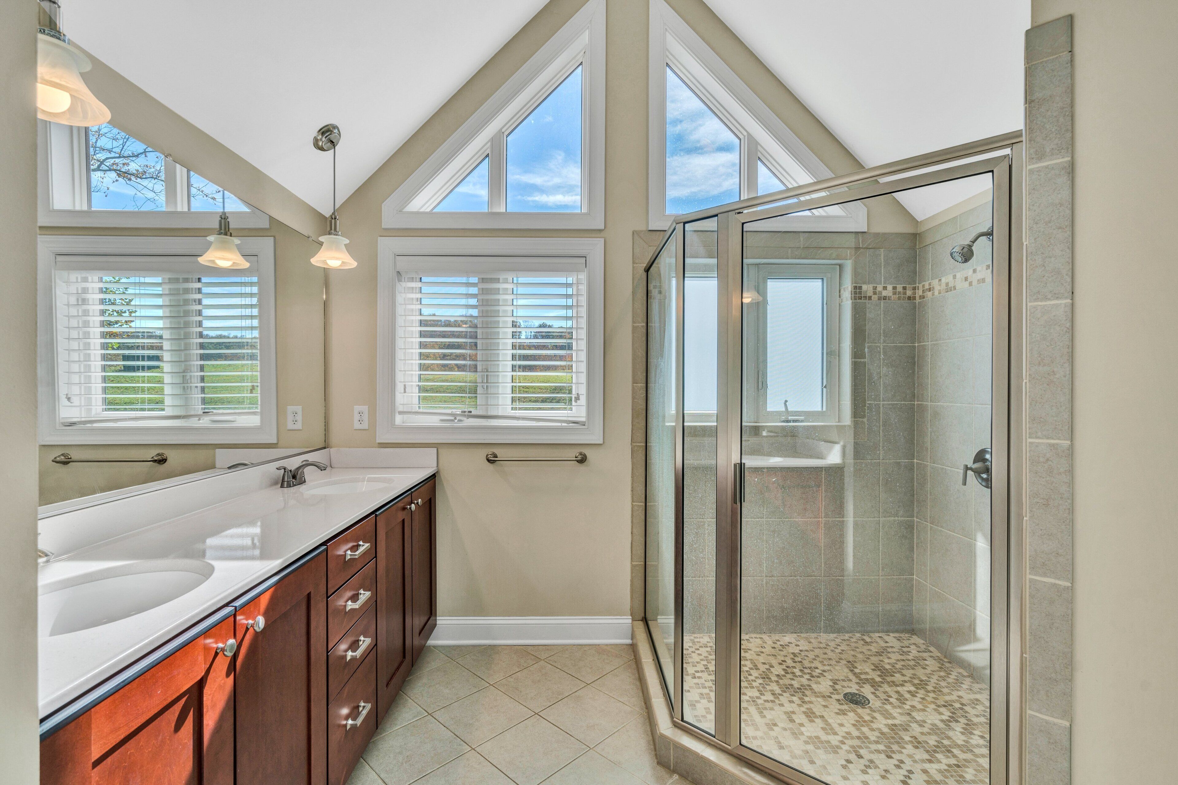 A bathroom with a glass-enclosed shower, a double sink vanity, and large windows.