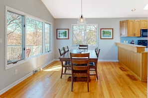 A dining area with a wooden table and chairs, large windows, and a kitchen with wooden cabinets. - The Lake House on Sunset Point - Lakefront Home With Private Dock & Pool Table (Moneta)