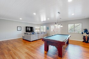 A spacious living room with a pool table, a sofa set, a television, and a large window. - The Lake House on Sunset Point - Lakefront Home With Private Dock & Pool Table (Moneta)