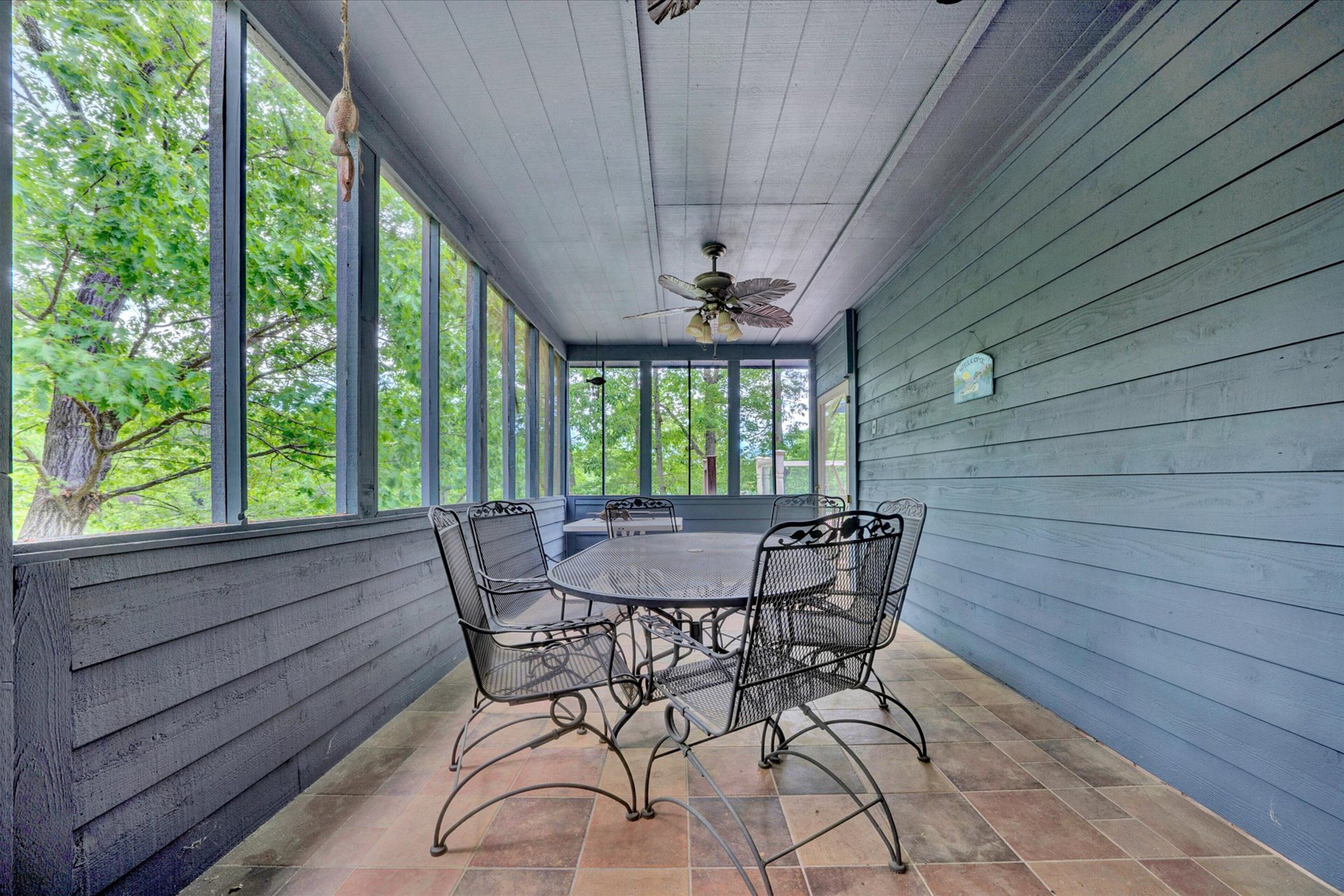 A covered patio with a table and chairs, large windows, and a ceiling fan.