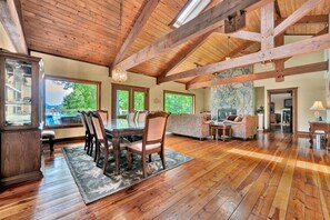 A spacious room with a wooden ceiling, large windows, a dining area with a table and chairs, and a stone wall. - The Main House - Lakefront Home With Private hot tub & Balcony (Huddleston)