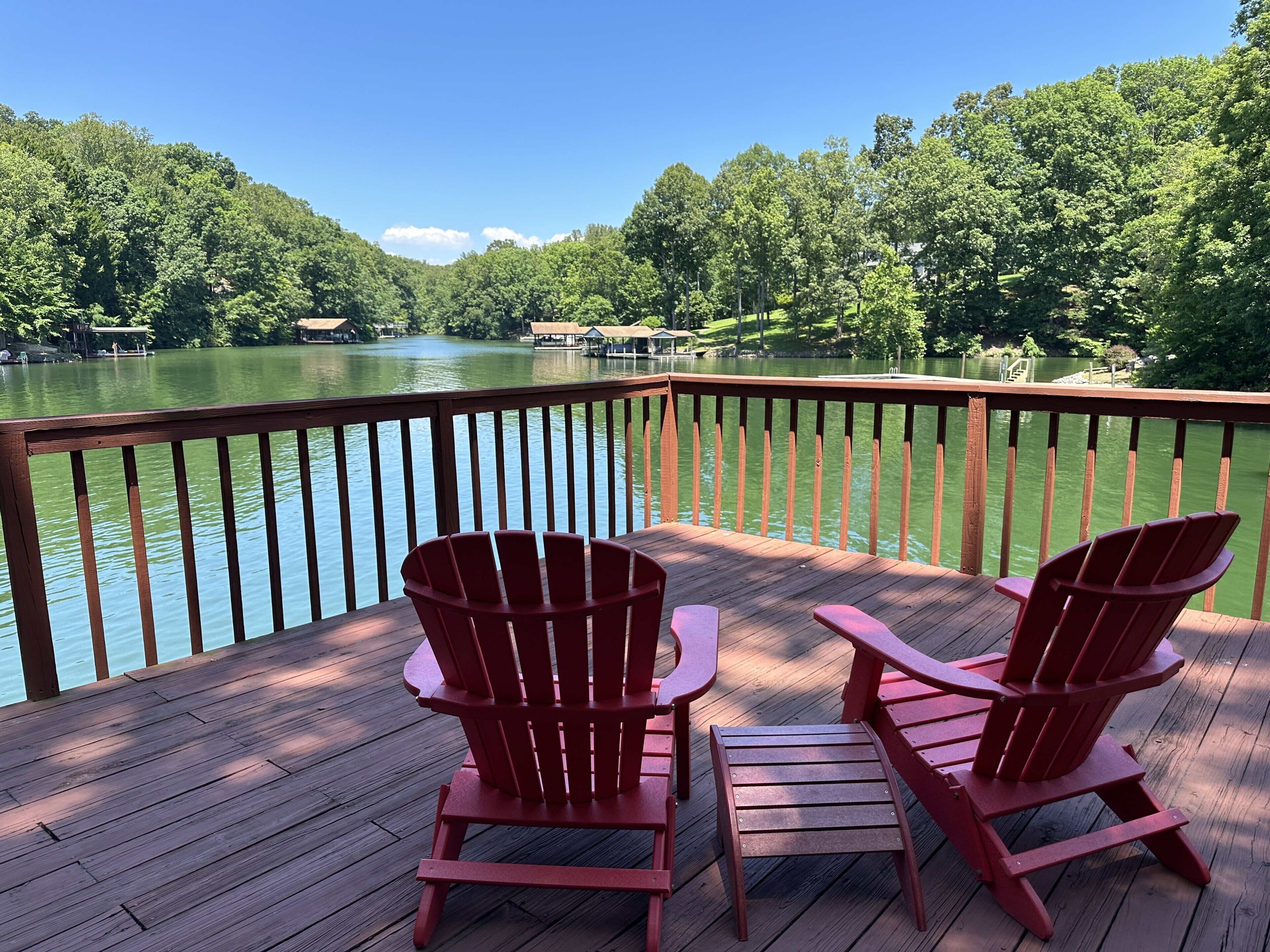 En träveranda med två röda Adirondack-stolar som är placerade så att de vetter mot en sjö, omgiven av träd.