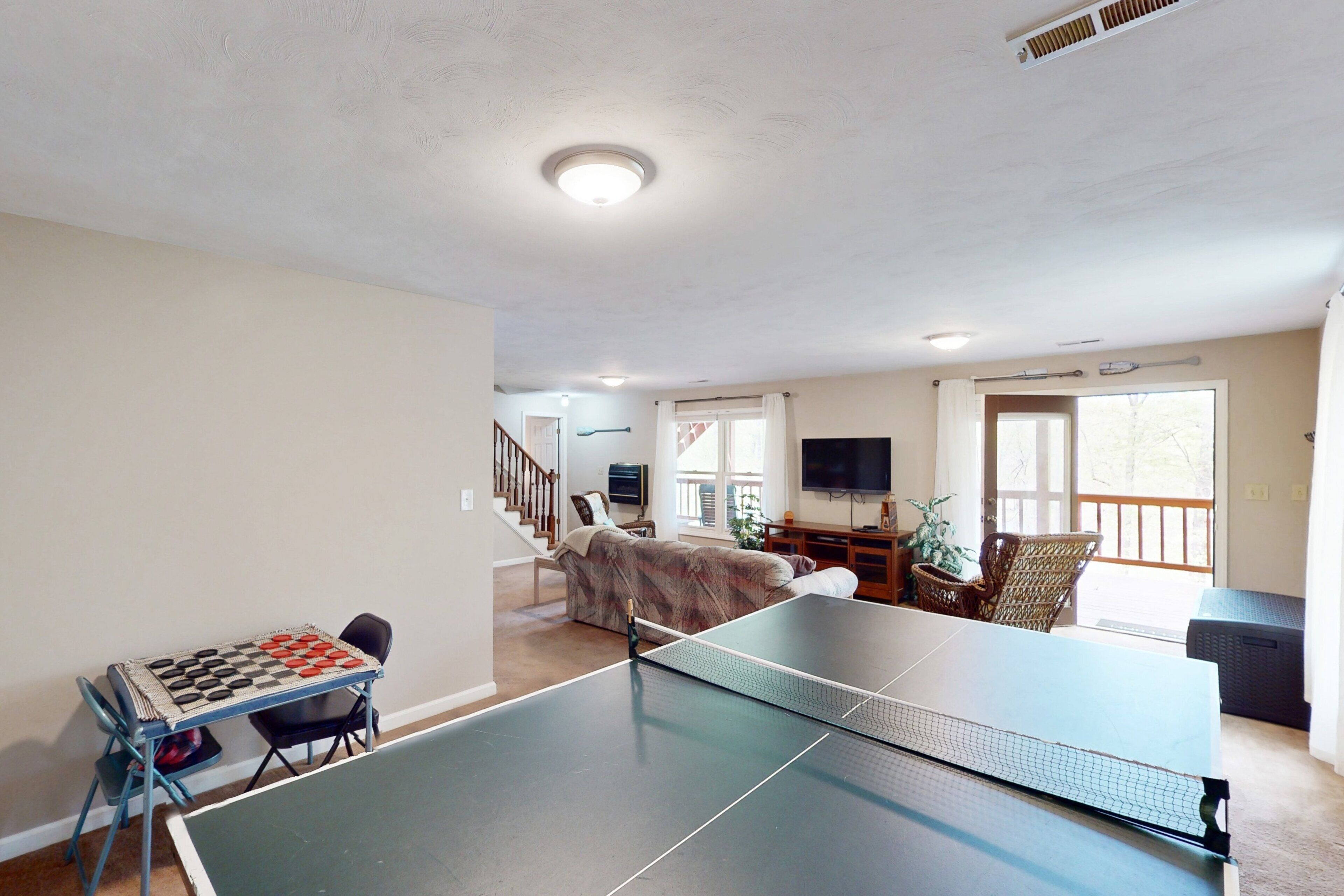 A ping pong table in a living room with a sofa, TV, and a staircase.
