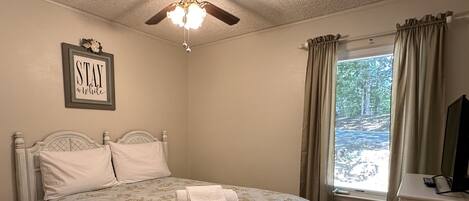 A bedroom with a bed, a ceiling fan, a window with curtains, and a bedside table.