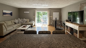 A living room with a sofa, coffee table, TV, and a view of the outdoors. - Humble Hideaway - Inviting Lakefront Home With Firepit, Balcony & W/D - Dog-friendly (Moneta)