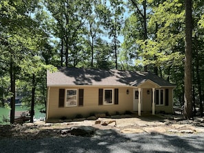 A small cabin with a single door and windows, surrounded by trees and a gravel path. - Humble Hideaway - Inviting Lakefront Home With Firepit, Balcony & W/D - Dog-friendly (Moneta)