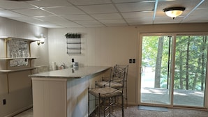 A kitchen with a marble backsplash, a bar area with stools, and a view of a forest through a sliding glass door. - Humble Hideaway - Inviting Lakefront Home With Firepit, Balcony & W/D - Dog-friendly (Moneta)