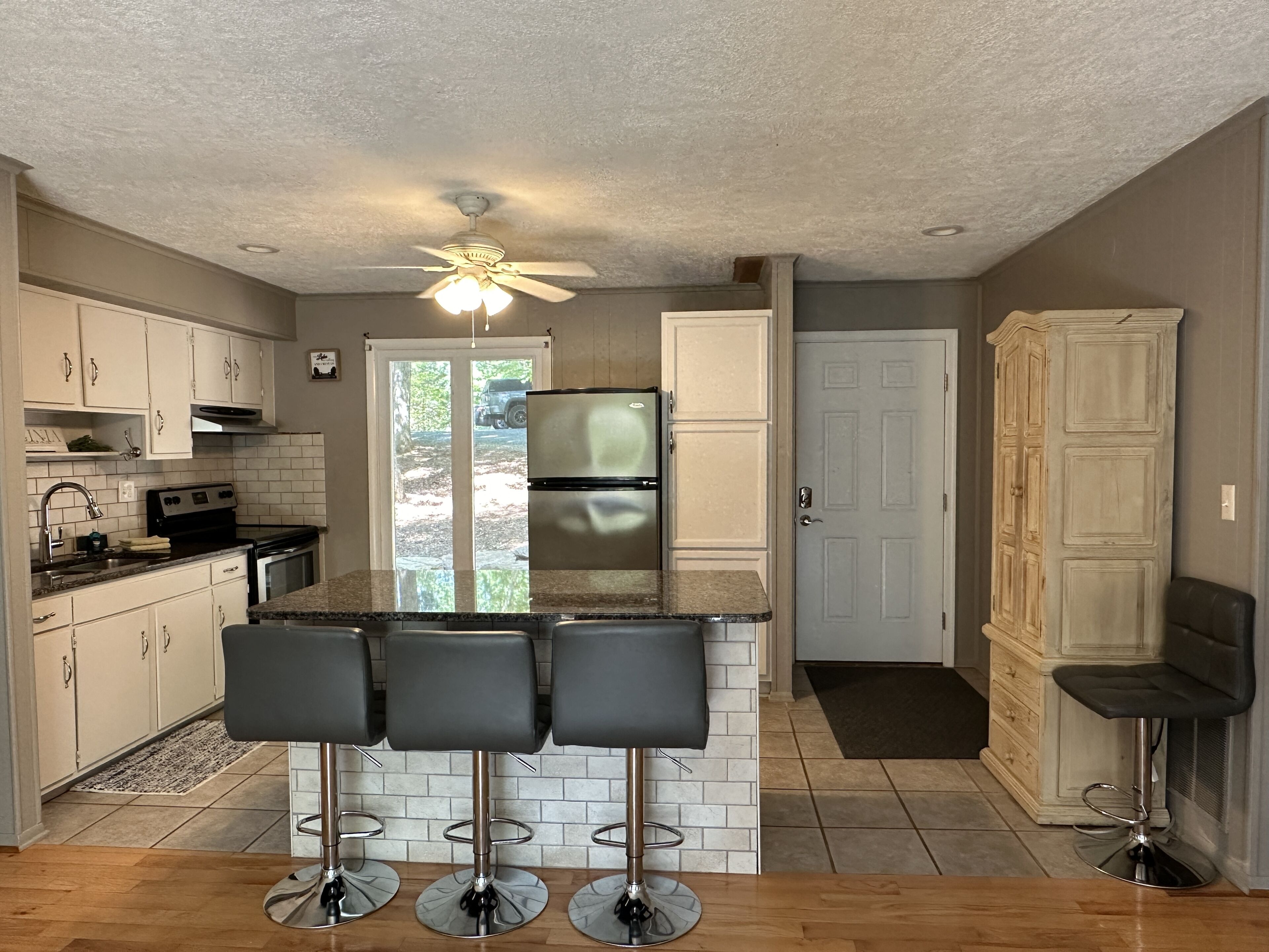 A kitchen with a central island, bar stools, a refrigerator, and a ceiling fan.