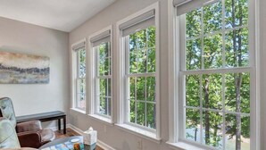 A room with large windows, a bench, a table with a book and a cup, and a painting on the wall. - Lakefront Tranquility - Lakefront Home With Views, Private hot Tub/dock, Deck, Free Wifi (Moneta)