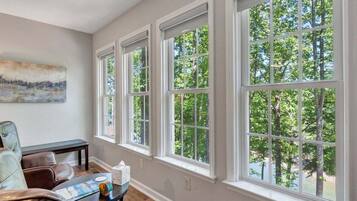 A room with large windows, a bench, a table with a book and a cup, and a painting on the wall.