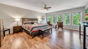 A bedroom with a bed, bedside tables, a chair, a desk, and large windows with a view of trees. - Lakefront Tranquility - Lakefront Home With Views, Private hot Tub/dock, Deck, Free Wifi (Moneta)