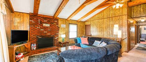 A living room with a fireplace, wooden ceiling beams, a television, and a sofa.